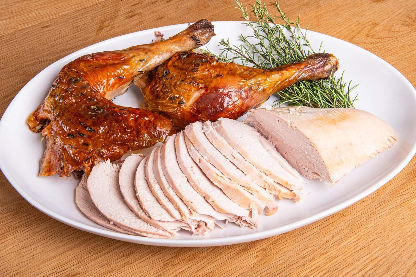 Carved turkey legs and sliced breast on a white plate with rosemary