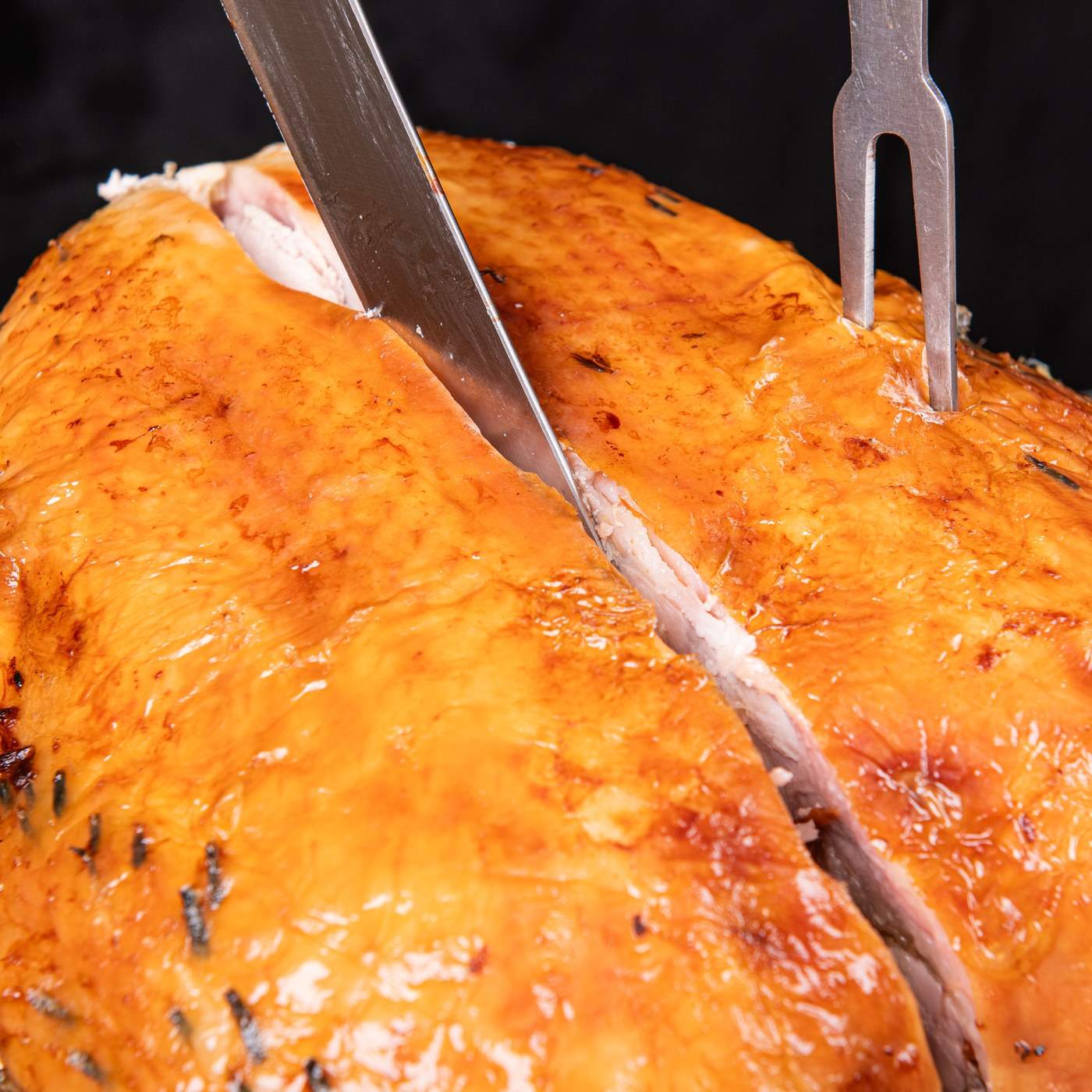 Slicing down through the breast of a roast turkey, held steady with a carving fork