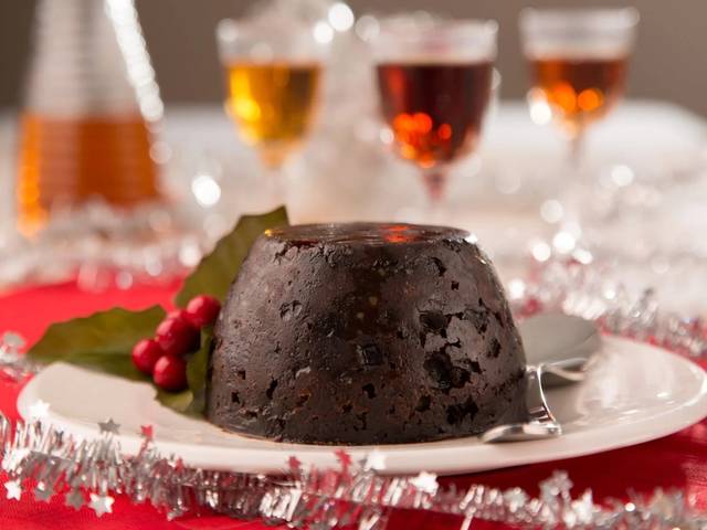 A dark Deluxe Christmas pudding on a white plate with holly
