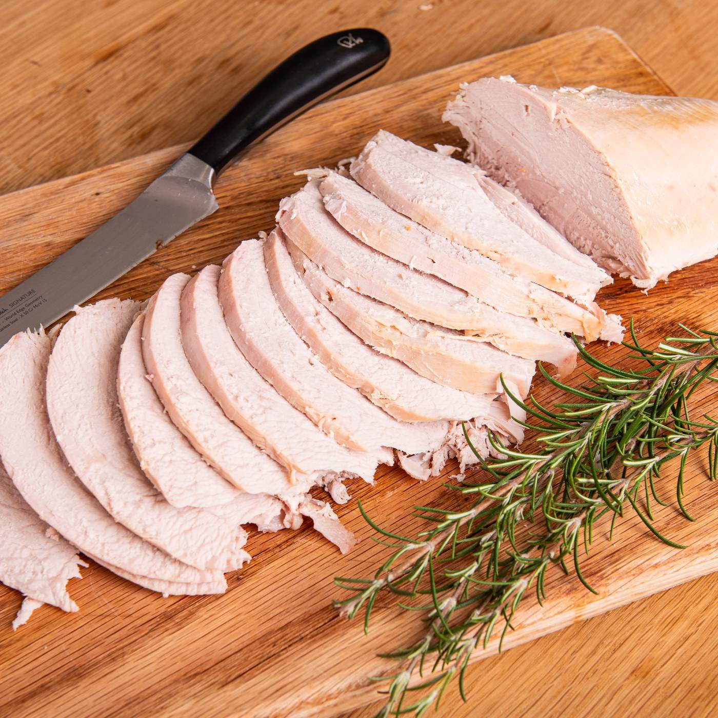 Neat slices of turkey breast on a wooden board with rosemary