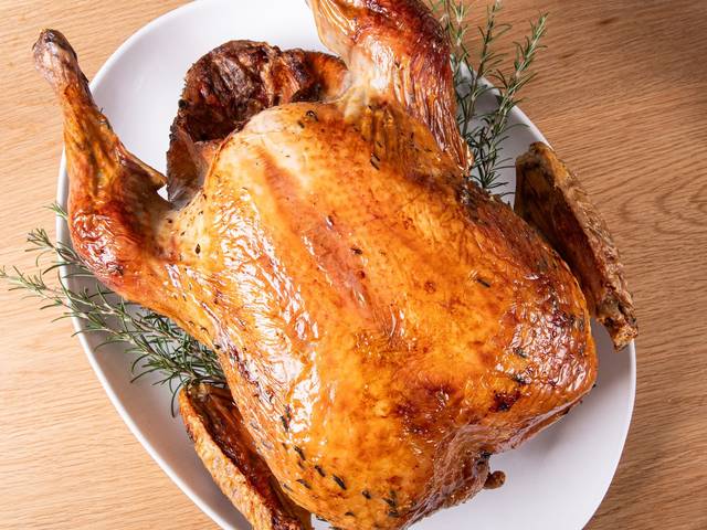 A whole roast Shropshire Bronze turkey on a white platter with rosemary